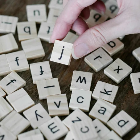 Vierkanten, houten blokjes met letters; een hand pakt het blokje met de letter 'j' erop